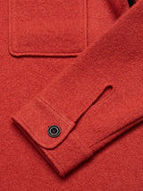 Close-up of the Blue de GĂȘnes Pampa Overshirt in Ochre Red, made from boiled wool. Features include a front pocket, buttoned cuffs with Corozo buttons secured by dark threads, and a soft, textured fabric with detailed stitching.