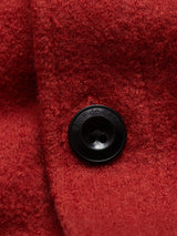 Close-up of the Pampa Overshirt in ochre red by Blue de GĂȘnes, featuring a large black Corozo button with a smooth, glossy finish and engraved text around its edge, perfectly complementing the textured boiled wool fabric.