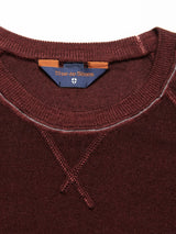 Close-up of the Marlon Knit - Prune sweater by Blue de Gênes, featuring a round neckline, raglan sleeves, and visible stitching. The Merino wool fabric showcases a textured reverse knit pattern for style and comfort. Inside label bears the Blue de Gênes shield logo.