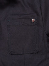 Close-up of the Amos Blazer - Dark Navy by Blue de Gênes: dark cotton canvas with visible stitching and a small circular cross shield pin accenting the pocket, showcasing the relaxed fit of this classic piece.