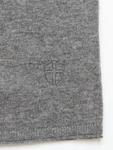 Close-up of the Monte AW Knit - Stormy Grey by Blue de Gênes, featuring a small embroidered shield emblem on soft, textured knit fabric neatly finished at the bottom.