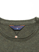 Close-up of the Monte AW Knit - Forest sweater made from Merino wool with a round neckline. Inside, it features the Blue de Gênes label and a decorative patch with a cross. The sweater is neatly finished at the edges.