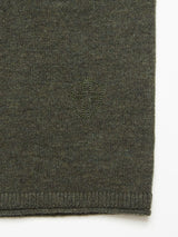 Close-up of Monte AW Knit - Forest by Blue de Gênes, showcasing textured green Merino wool fabric with a subtle embossed shield emblem on the left side and a visible finished seam at the bottom right, typical of a crewneck jumper.