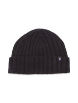 The Oscar Croft beanie by Blue de Gênes is a luxurious dark navy, 5-gauge knit with a ribbed design and folded brim. It features a small logo tag with a shield and cross emblem on the brim against the crisp white background.