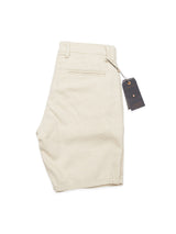 A pair of Blue de Gênes Abramo Desk Shorts - Natural, made from a cotton/linen blend, is neatly folded with a black tag attached. They feature one back pocket with subtle seam detail and visible belt loops.
