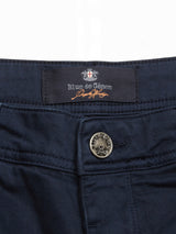 Close-up of Paulino Cargo Shorts in navy, showcasing a button with embossed text and a Blue de Gênes label. Crafted from military cotton, the label displays a subtle emblem with orange stitching on a black background.