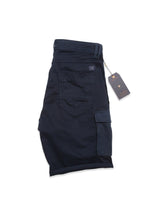 A folded pair of Blue de Gênes Paulino Cargo Shorts in dark navy, crafted from military cotton, with a visible utility pocket and sewn-on label. A cardboard tag is attached with a string, all resting on a white surface.