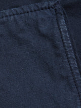 A close-up of the Paulino Cargo Shorts - Navy by Blue de Gênes shows a dark blue fabric with a subtle grid pattern and diagonal seam, highlighting the texture and stitching reminiscent of military cotton and evoking the rugged appeal of utility pockets.