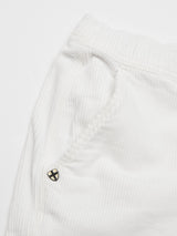 Close-up of the Crivello Cord Shorts in Snow White by Blue de Gênes, showcasing a loose fit and visible side pocket near the waistband. A small black and gold shield-shaped emblem adorns the fabric with fine vertical ridges, adding a garment-dyed charm.