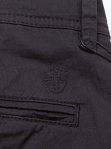 Close-up of Menzino Shorts - Dark Navy by Blue de Gênes, featuring a stitched shield emblem above a horizontal-slit pocket with a belt loop. The fabric reveals a subtle textured herringbone pattern.