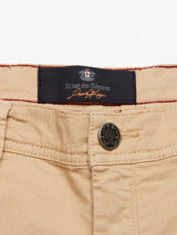 Khaki Menzino Shorts from Blue de Gênes feature a leather button, a Blue de Gênes label on dark fabric with decorative stitching, crafted from garment-dyed herringbone fabric with visible belt loops.
