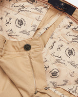 A close-up of the open zipper and button on the Menzino Shorts - Khaki by Blue de Gênes reveals an inner lining with cursive script, anchor illustrations, and circular emblems, suggesting a garment-dyed finish that enhances the rich texture of the herringbone fabric.
