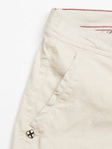 Close-up of Menzino Shorts - Stone by Blue de Gênes, crafted from herringbone fabric with a focus on the pocket area. The texture features a black and silver button detail near the pocket and a hint of red stitching inside the garment-dyed waistband.