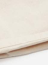 Close-up of the Menzino Shorts in Stone by Blue de Gênes, showcasing a beige, garment-dyed fabric with a horizontal seam near the bottom. The soft texture hints at herringbone, reminiscent of chino shorts, against a light neutral background.