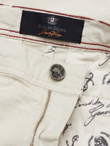 Close-up of the Menzino Shorts - Stone by Blue de Gênes reveals a button with the brand label above the zipper. The inner herringbone fabric features nautical and cursive designs, adding sophistication to this classic piece.