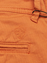 Close-up of the Menzino Shorts - Apricot by Blue de Gênes, highlighting the orange herringbone fabric with a stitched shield emblem. Features include a button loop, slit pocket, and visible garment-dyed texture showcasing weaving and stitching details.