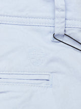 Close-up of the Menzino Shorts - Blue Water by Blue de Gênes, showcasing light blue garment-dyed fabric with a cross-stitched emblem. Features include belt loops, a pocket, and a black plastic tag.