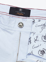 Close-up of light blue Menzino Shorts - Blue Water by Blue de Gênes, showcasing a visible zipper, silver button, label, red stitching on the waistband, and inner fabric with decorative script and crest designs—highlighting the meticulous craftsmanship of these garment-dyed beauties.