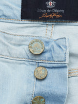Close-up of Repi Tocco Jeans in bleach denim by Blue de Gênes, showcasing a prominent brand label on the waistband. Features three rustic metal buttons and comfort stretch fabric, revealing texture and stitching details that highlight craftsmanship.