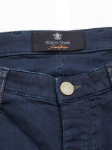 Close-up of Repi Grasso Jeans in navy, a regular slim-fit with classic five pockets and a brass button. Above the button is a Blue de Gênes label with an emblem. Visible stitching along the waistline highlights meticulous craftsmanship.