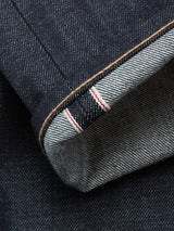 Close-up of the Blue de Gênes Giacomo Selvedge V2 Jeans in raw dark blue denim, featuring a cuffed hem that highlights the white inner selvedge seam with a distinctive red line and showcases the textured weave.