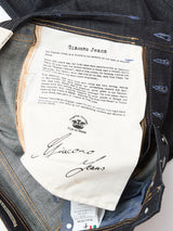A close-up of the Giacomo Selvedge V2 Jeans - Raw Denim by Blue de Gênes, made in Italy, showing a printed label with brand story, logo, and signature on white fabric sewn inside the denim waistband and pocket area.
