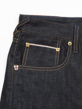 Close-up of Blue de Gênes Giacomo Selvedge Jeans in raw denim featuring contrast stitching, a small front pocket with a stitched accent, and metal rivets. Italian craftsmanship is highlighted by an emblem resembling a shield with a cross near the pocket.