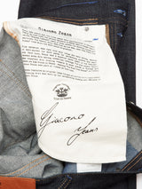 Close-up of a Blue de Gênes label on a cream patch inside dark blue Giacomo Selvedge Jeans - Raw Denim, celebrating Italian craftsmanship and fabric quality, with a signature at the bottom.