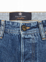 Close-up of Giacomo Maracas Jeans in a relaxed fit, highlighting Italian craftsmanship. The visible waistband label shows Blue de Gênes. These jeans have an orange stitched buttonhole, a detailed metal button, and feature a classic vintage wash with slight wrinkles.
