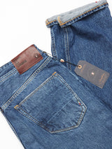 The Giacomo Maracas Jeans - Vintage Wash by Blue de Gênes are relaxed fit, folded blue jeans exemplifying Italian craftsmanship with visible stitching, a brown leather waistband patch, a small back pocket detail, and slightly rolled cuffs.