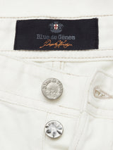 Close-up of white denim Giacomo Bull WTH by Blue de Gênes, showcasing the label with a cross emblem above the fly. Two metallic buttons embossed with the brand name highlight these pants, exemplifying Italian craftsmanship.