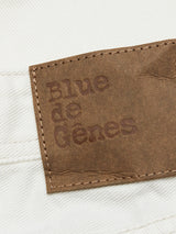 A close-up of a leather label sewn onto white denim fabric with Blue de Gênes embossed, showcasing Giacomo Bull WTH - White Denim jeans. The contrasting stone-washed brown label and white background reflect timeless style, often crafted in Italy.