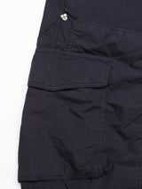 Close-up of the Mustang Cargo Pant - Navy by Blue de Gênes, featuring dark blue parachute cotton fabric with visible seams, a fold-over utility pocket, and a small metallic triangular logo with a white cross above it. The fabric looks textured and slightly crumpled.