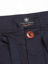Close-up of the Mustang Cargo Pant in navy featuring parachute cotton, a brown button, Blue de Gênes label, textured finish, utility pockets, and a stitched waistband detail.
