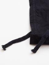 A close-up of the Mustang Cargo Pant - Navy by Blue de Gênes features dark fabric with braided drawstrings extending from the edge, reminiscent of cargo pants. The drawstrings have frayed ends, and the parachute cotton fabric is set against a neutral background.