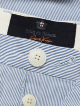 Close-up of the Palto Riga Chino - Blue Stripe by Blue de Gênes, featuring a blue and white striped design in soft cotton. A white button adds detail, and the black interior label displays Blue de Gênes in orange script.