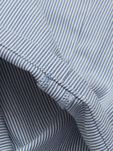 Close-up of the Palto Riga Chino by Blue de Gênes, featuring blue and white striped cotton fabric with detailed stitching along the seam. The slightly wrinkled material highlights the relaxed fit and texture.