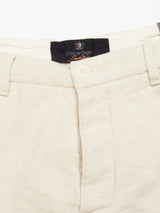 Close-up of the Blue de Gênes Palto Desk Chino in a coarse, natural beige cotton/linen blend with a buttoned waistband. A black label with white and orange text is partially visible on the inside. These pants offer a relaxed fit, perfect for casual wear.