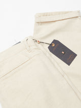 Blue de Gênes Palto Desk Chino in Natural, crafted from a cotton/linen blend with belt loops and back pockets, are neatly folded on a white background. A dark gray tag with orange writing, attached via a metal eyelet and black string, highlights their relaxed fit.