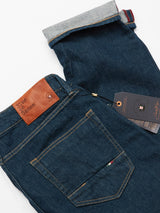 Crafted in Italy, the dark blue Vinci Topaz Jeans by Blue de Gênes feature a brown leather patch labeled Blue de Genes on the back pocket. With comfort stretch denim, one leg is partially rolled to reveal a striped cuff and a tag with branding details is attached.
