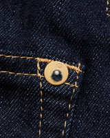 Close-up of dark blue denim fabric from Blue de Gênes Cosimo Trucker Jacket, featuring a pocket seam with yellow stitching. A metal rivet near the seam highlights the texture and detail of this classic western jackets material.