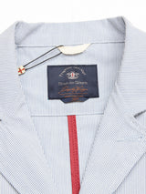 Close-up of a blue pinstriped Gabbiano Riga Blazer collar by Blue de Gênes, showing interior details. A black label reads the brand name, with decorative stitching and a tag featuring a cross emblem near the neckline, crafted from cotton yarn dye stripe fabric for a relaxed fit.