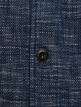 The Kojima Jacket - Navy by Blue de Gênes features a textured blue and white woven pattern inspired by Japanese workwear, highlighted by a central black plastic button. Its checkered design and visible threads create an intricate, lived-in appearance.