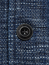 Close-up of the dark blue and white textured Kojima Jacket - Navy by Blue de Gênes. It features a black button embossed with the brand name, secured by dark thread. The fabrics weave gives it a lived-in look, reminiscent of Japanese workwear.