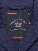 Close-up of a navy garment label with orange stitching. The label reads “Progetto Heritage” and “Blue de Gênes,” featuring a crest with two lions and a shield. Crafted from textured cotton, the Gervaso Tarlo Blazer exemplifies quality and tradition, ideal for any sophisticated collection.