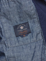 A close-up of denim fabric features a sewn label reading Blue de Gênes with extra text and a red 50 below. The lightly worn cotton showcases blue variations, complemented by corozo buttons charm. The item is the Gervaso Tarlo Blazer in Navy from Blue de Gênes.