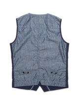 The Ludovico Tarlo Gilet - Navy by Blue de Gênes is a sleeveless light blue denim vest with dark blue trim and a chambray texture. It features two small black buttons on each side near the bottom, a straight hem, and a subtle center slit, echoing the classic Navy Cotton Gilet design.