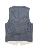The Pantella Desk Gilet by Blue de Gênes, in denim blue, features a textured Cotton/Linen blend, a beige lining, corozo buttons, and a metal buckle waist adjustment. Its back is elegantly longer and tapers to two points.