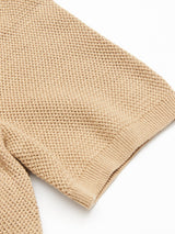 Close-up of a Filo Knit Polo - Khaki by Blue de Gênes, showcasing its beige waffle-knit sleeve made from 100% cotton. The textured fabric is set against a white background, emphasizing the intricate knit pattern and ribbed cuff.