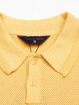 The Filo Knit Polo - Yellow Grain by Blue de Gênes is a 100% cotton shirt with a collar, three buttons, and retro repeat stitch, giving it a stylish knitted look.